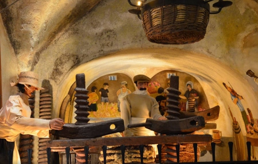 exhibit shows men turning grape press wheel at 'Koutsoyannopoulos Wine Museum'